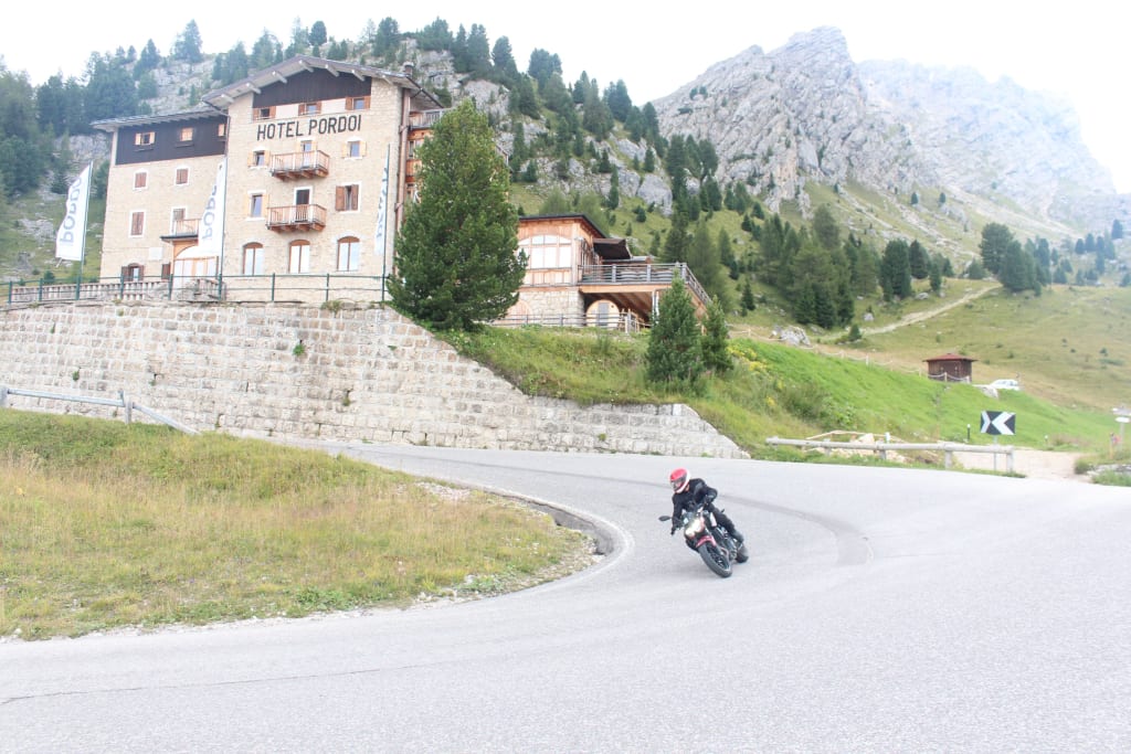 Motorcycle rider on winding mountain road near Hotel Pordoi and rocky cliffs