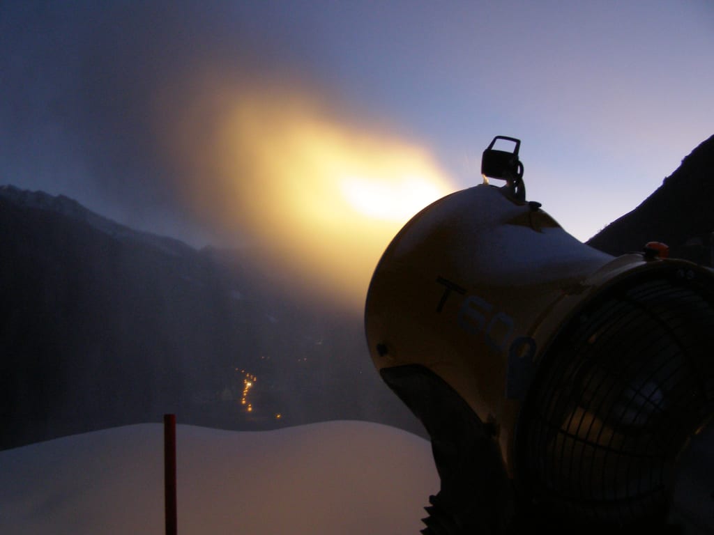 Schneekanone stößt Nebel in verschneiter Berglandschaft aus bei Abendlicht