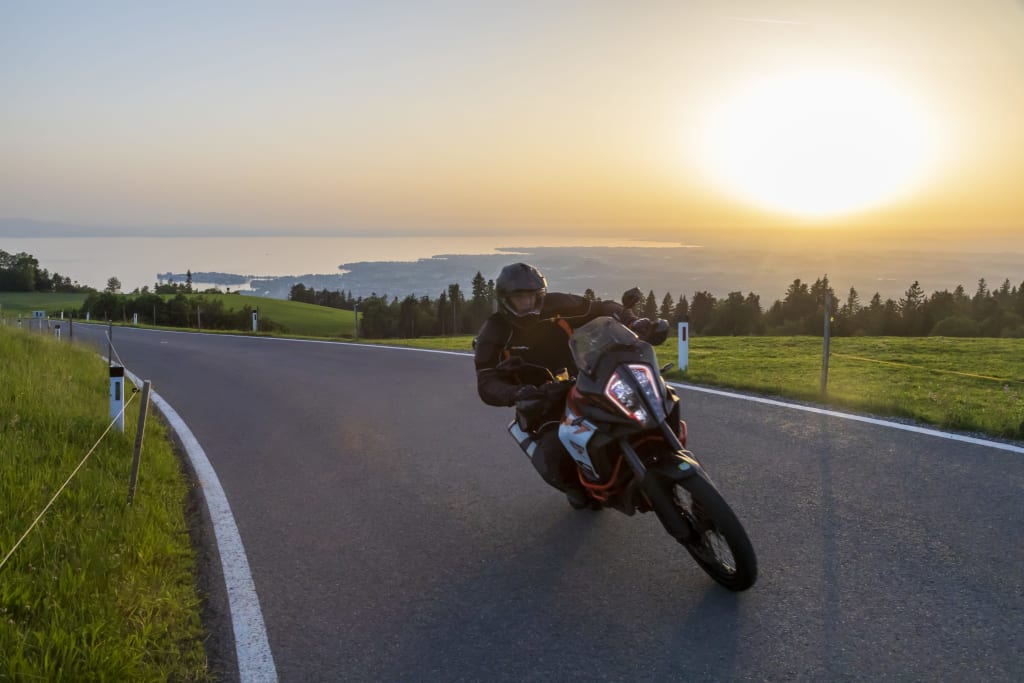 Motorradfahrer fährt bei Sonnenuntergang auf kurviger Landstraße