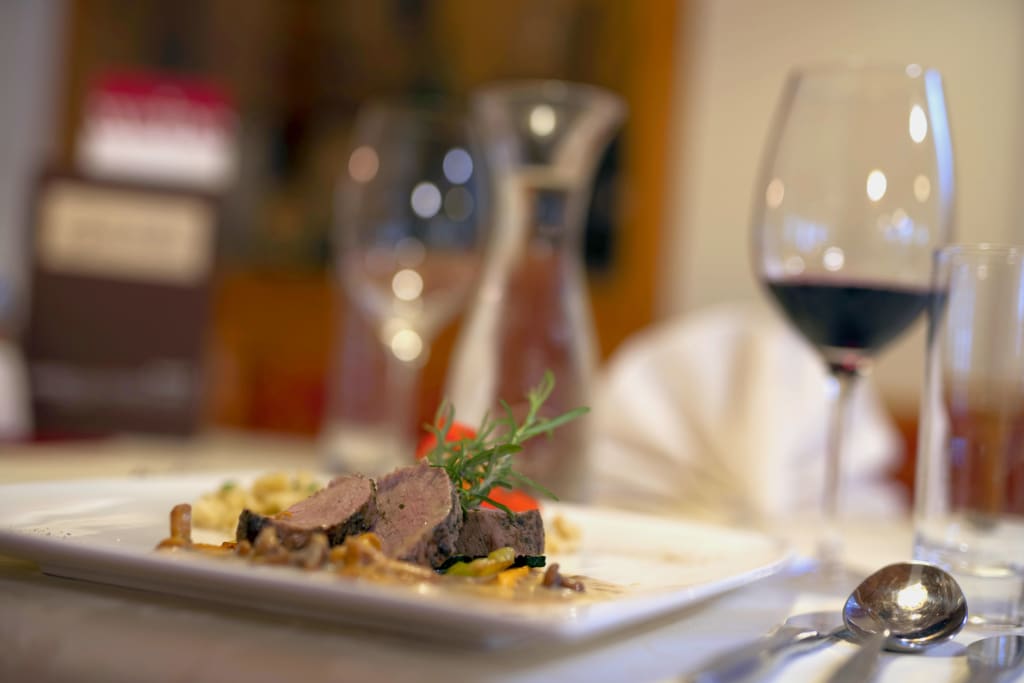 Fein angerichtetes Fleischgericht mit Rotwein und Besteck auf einem gedeckten Tisch