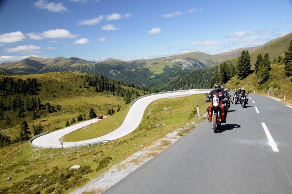 Motorradfahrer fahren eine kurvige Bergstraße bei sonnigem Wetter