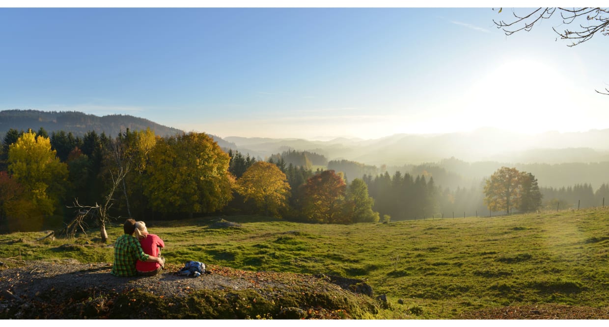Paar sitzt auf einem Felsen und blickt auf nebligen Wald im Sonnenuntergang