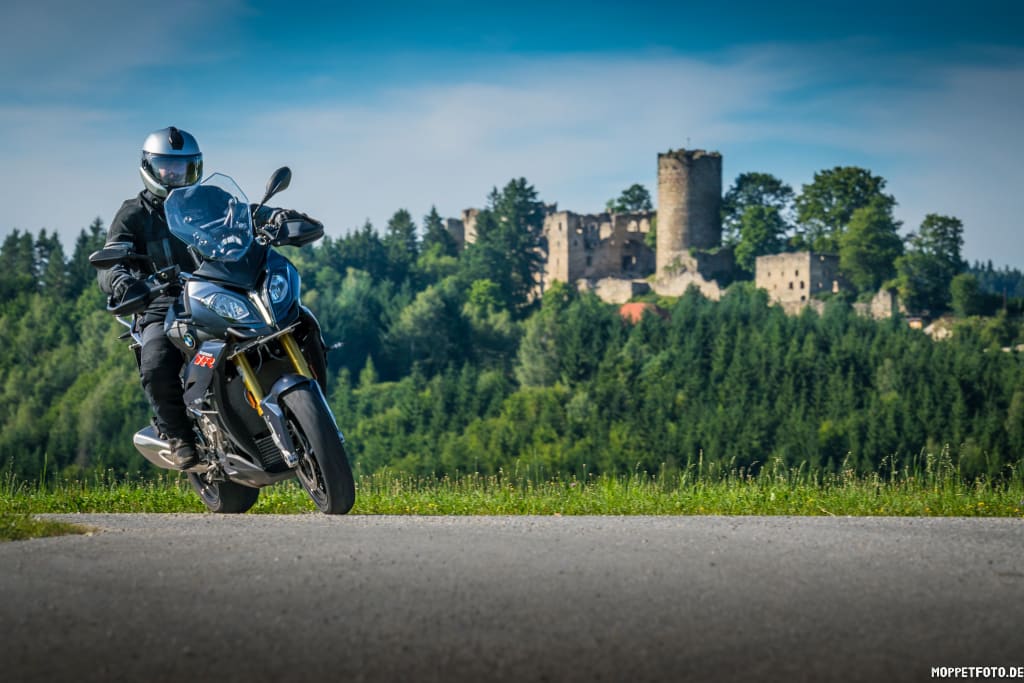 Motorradfahrer auf Straße vor Wald und Burgruine bei klarem Himmel