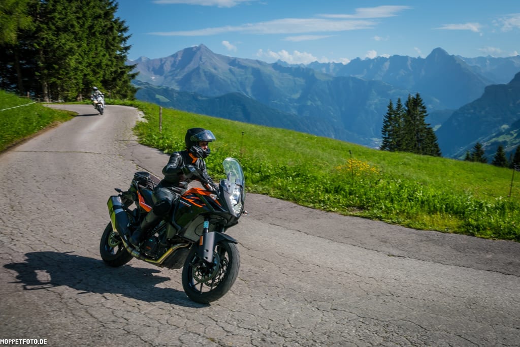 Motorradfahrer auf Bergstraße mit Alpen im Hintergrund