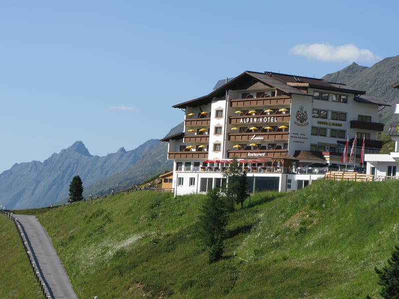 Alpenhotel auf einer grünen Bergwiese mit Bergen im Hintergrund
