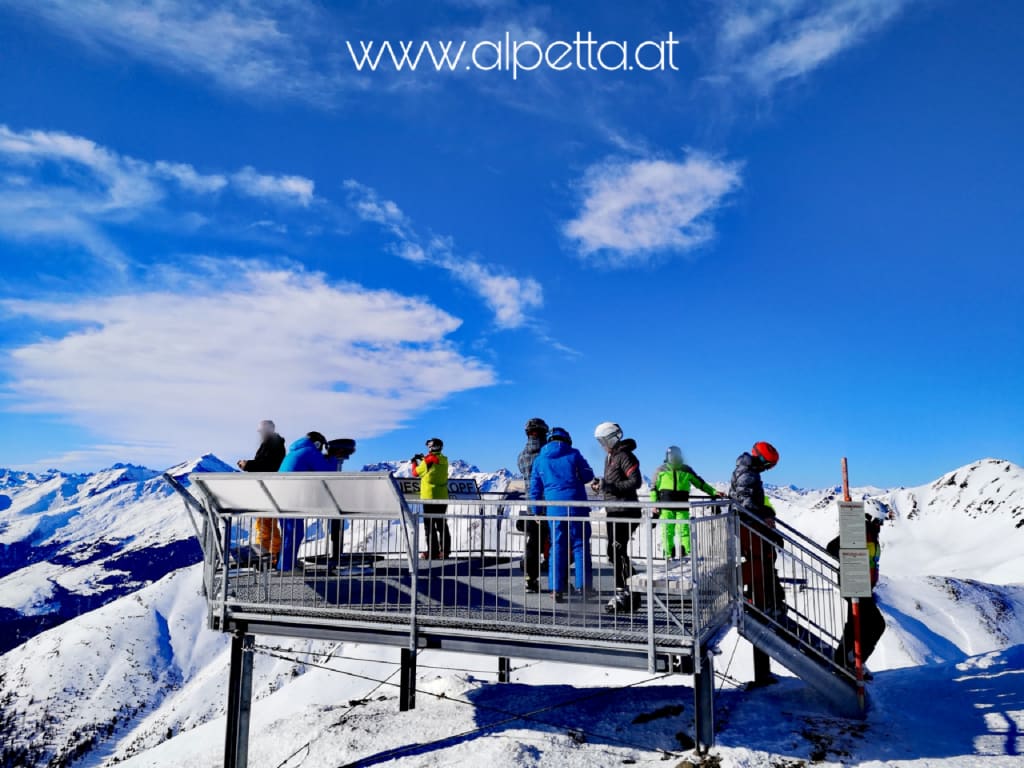 Uitkijkplatform met skiërs bij besneeuwde bergen en blauwe lucht