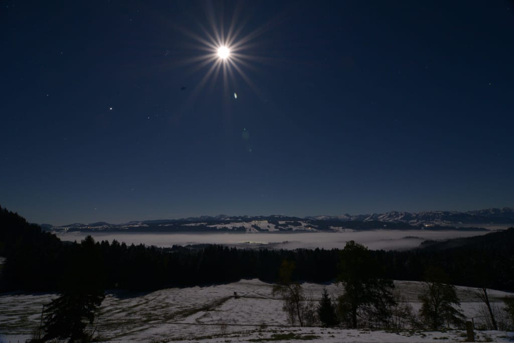 Mondschein über schneebedeckter Landschaft mit Bergen im Hintergrund