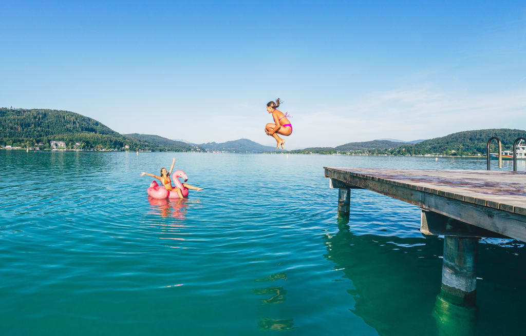 Woman jumping off pier into lake, another on flamingo float