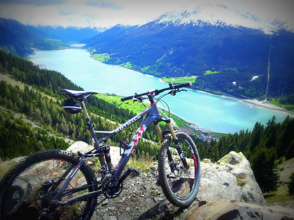 Mountainbike op bergpad met uitzicht op meer en besneeuwde bergen