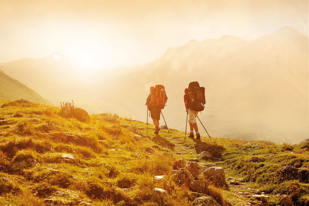 Aktivurlaub für Erlebnissammler - 7 Nächte Zwei Wanderer mit Rucksäcken wandern auf einem Bergpfad im Sonnenlicht