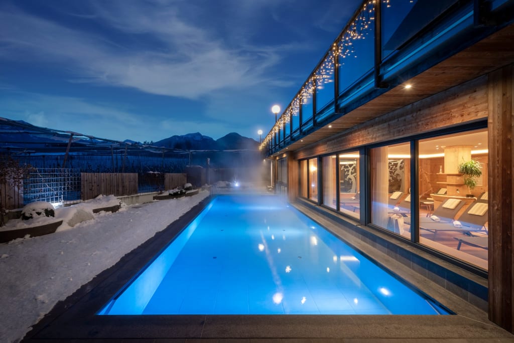 Beheizter Außenpool neben modernem Gebäude bei Nacht mit Schnee und Bergen