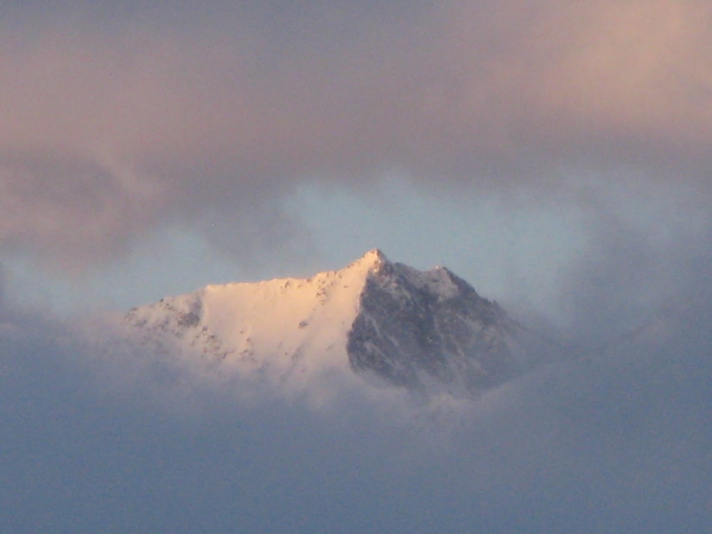 Schneebedeckter Berggipfel umgeben von Wolken bei Sonnenuntergang