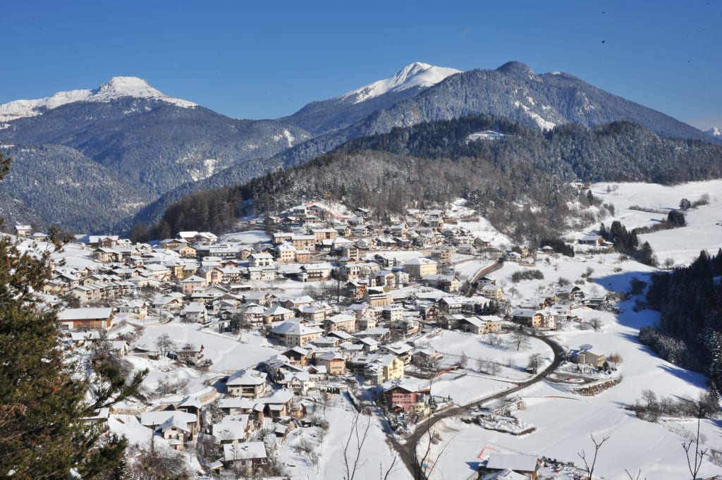 Schneebedecktes Dorf in einem Tal vor schneebedeckten Bergen